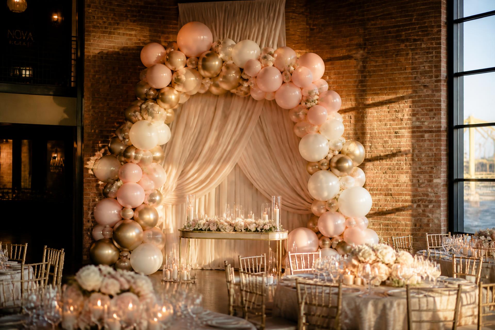 Blush and gold balloon arch framing a draped backdrop at a Pittsburgh event designed by Be A Little Extra